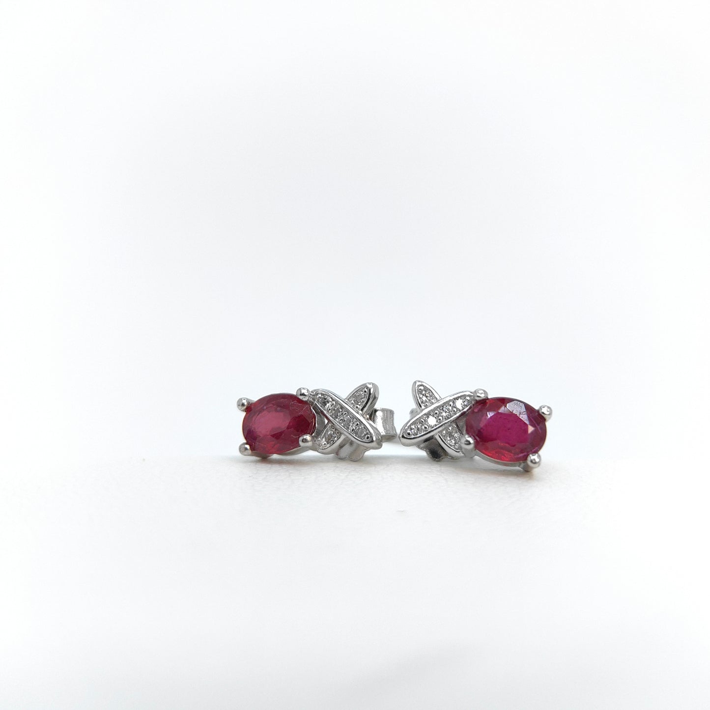 Pair of earrings with red gemstones and silver X-shaped designs on a white background