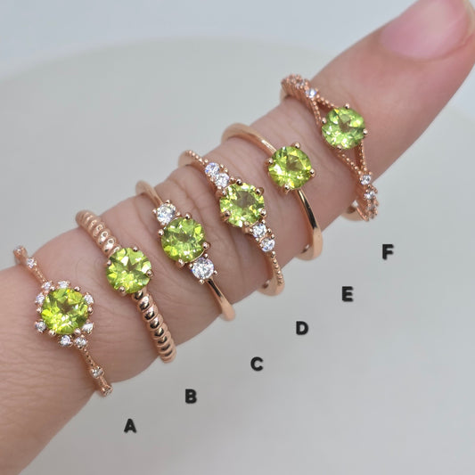 Set of gold rings with green gemstones on a finger against a white background