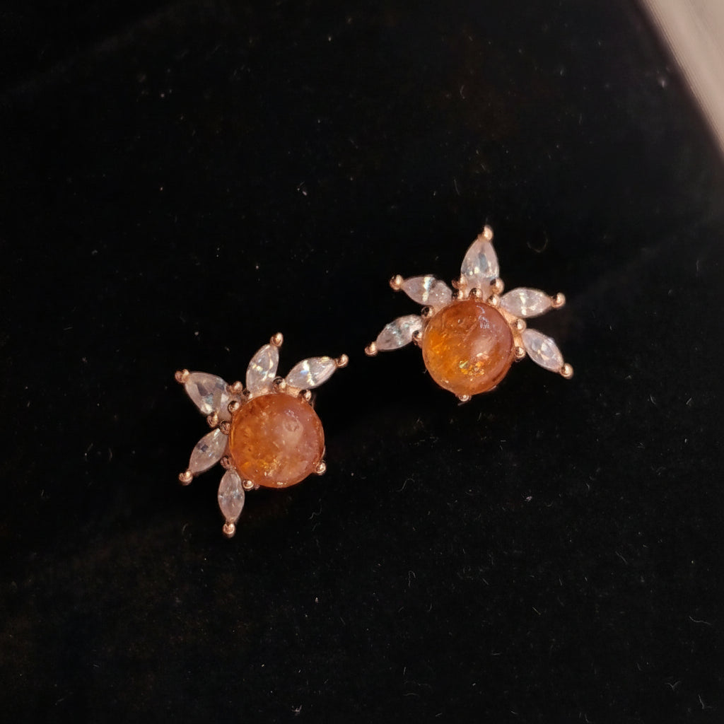 Pair of sunflower-shaped earrings with brown centers and diamond-like stones on a black background