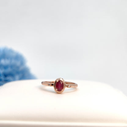 Gold ring with a red gemstone on a white surface with a blurred blue object in the background