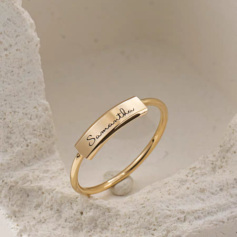 Gold ring with engraved name on a textured surface