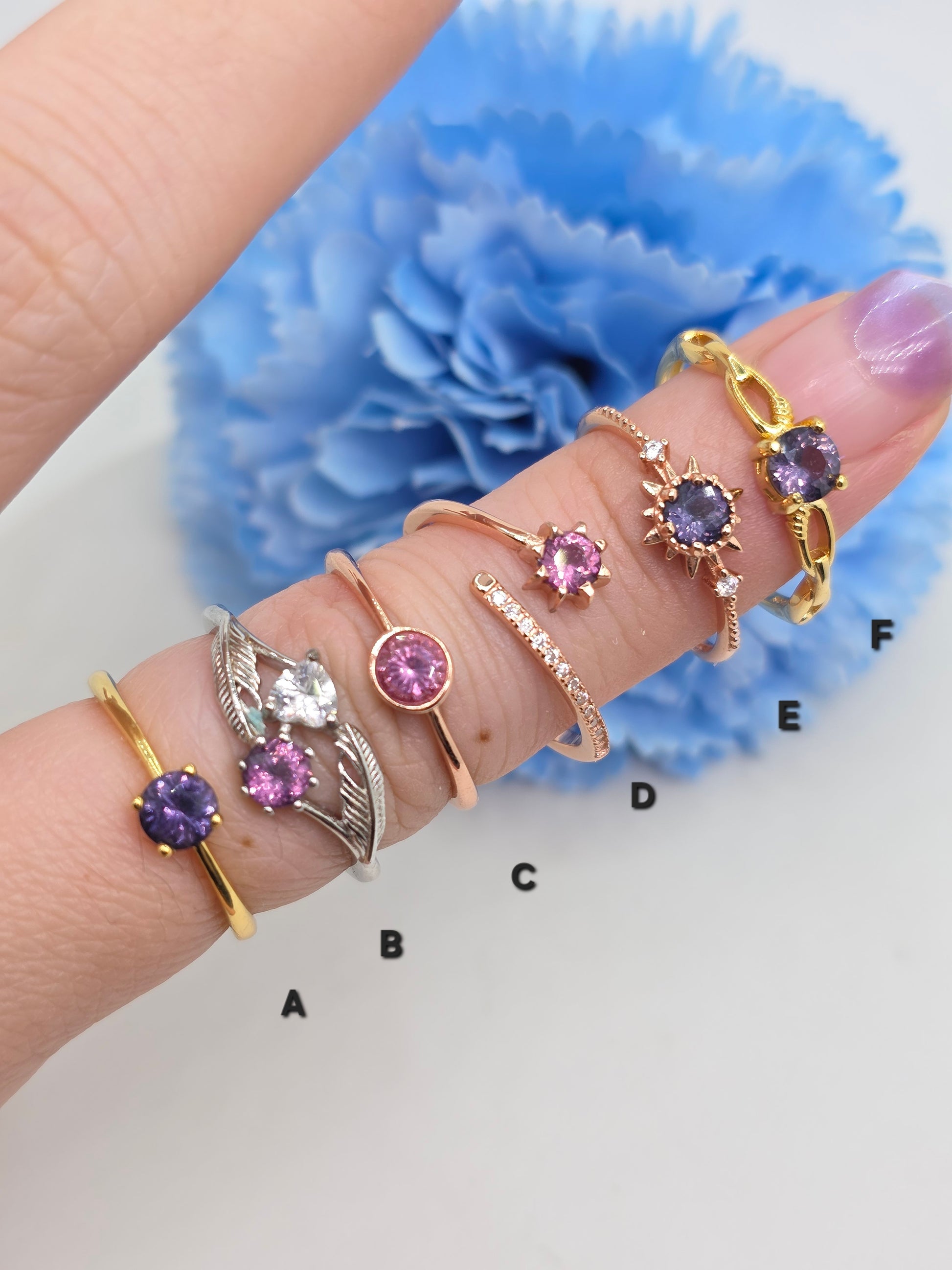 Hand wearing multiple rings with gemstones against a blue flower background