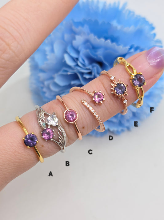 Hand wearing multiple rings with gemstones against a blue flower background