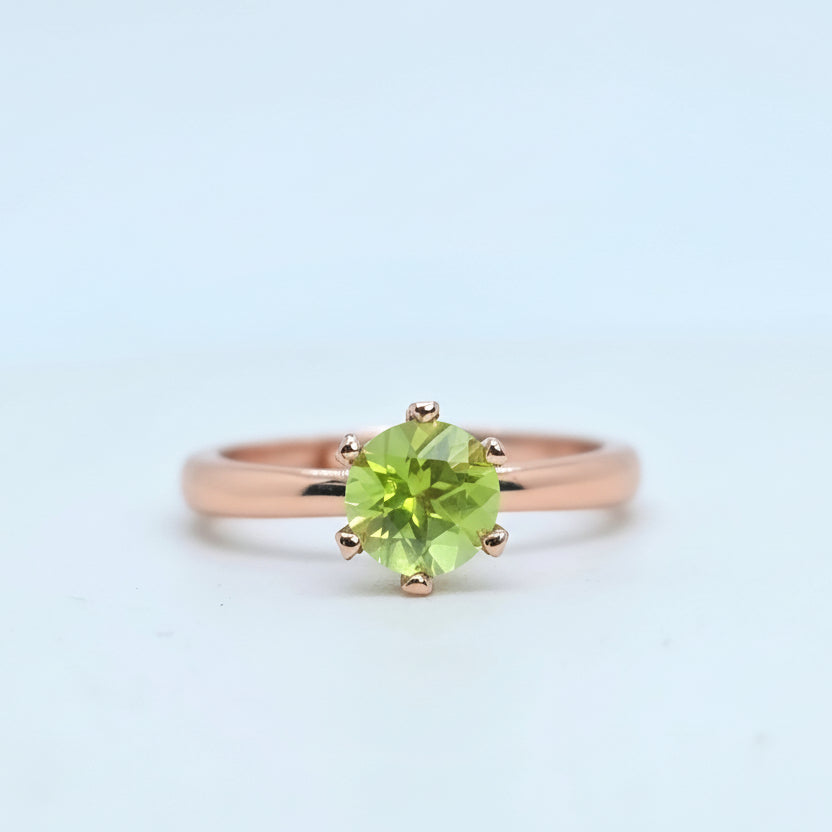 Rose gold ring with a green gemstone on a light blue background
