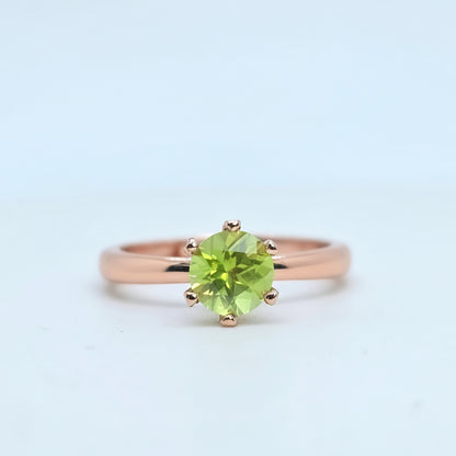 Rose gold ring with a green gemstone on a light blue background
